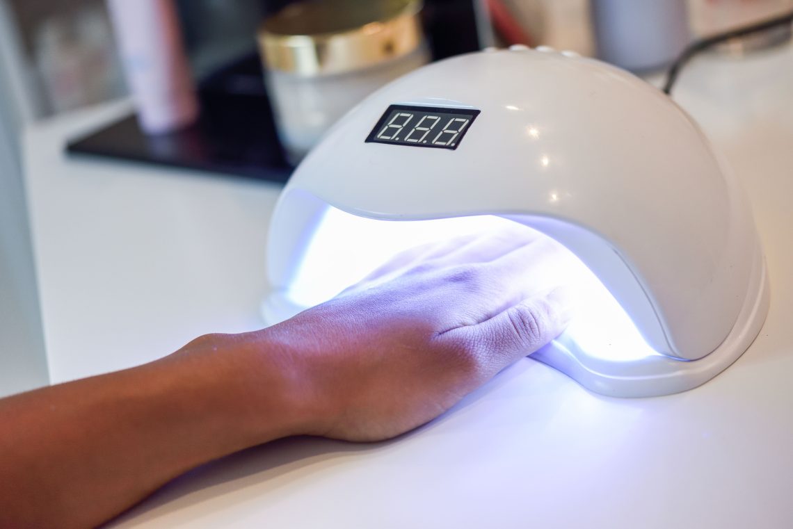 dłoń włożona pod lampkę UV u kosmetyczki